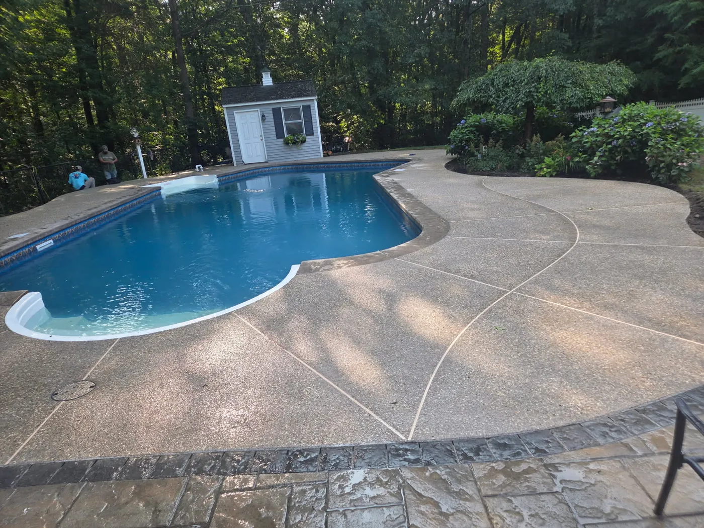 Exposed aggregate pool deck with curved saw cut lines and a stamped border