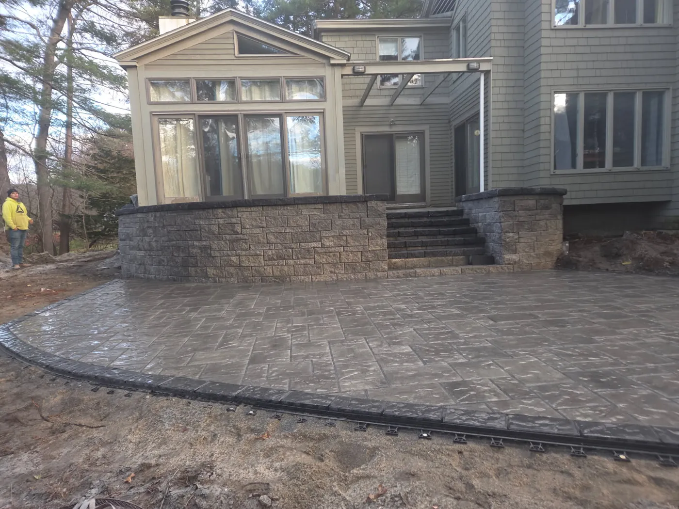 Stamped concrete patio with a stone faced wall and steps below a sunroom